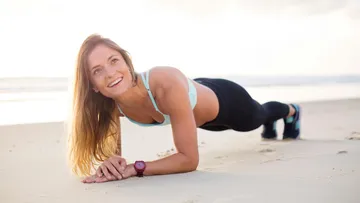 Woman planking on sandy beach, smiling.