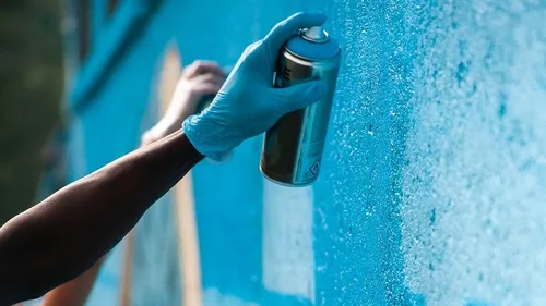 Blaues Graffiti mit der Hand auf die Wand sprühen.