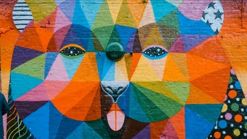 Colorful geometric bear face mural on brick wall.