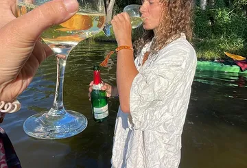 Person, die aus einem Weinglas am See trinkt.