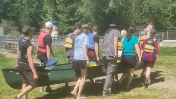 Group carrying a canoe on grassy area.