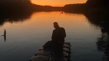 Person sitting on dock at sunset by lake.