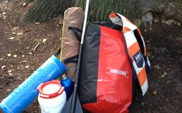 Camping gear against a tree on forest ground.