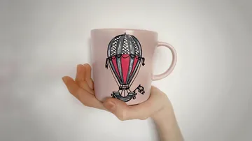 Hand holding mug with balloon design.