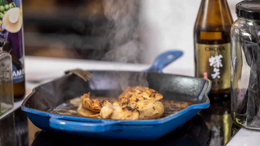 Chicken cooking in a blue skillet on stove.