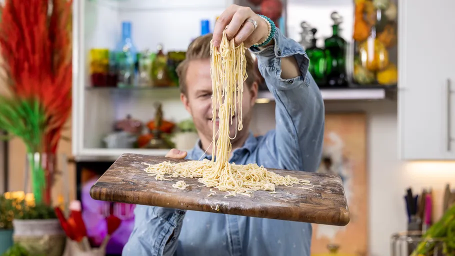 Person holding spaghetti with wooden board in kitchen.