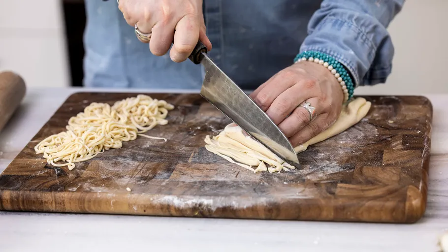 Person cutting homemade pasta on wooden board.