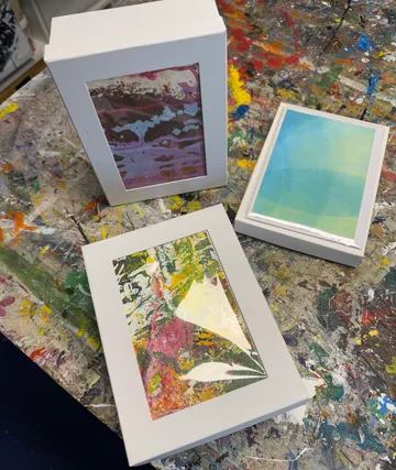 Three framed abstract paintings on splattered table.
