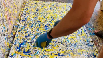 Person, die abstrakte Kunst mit Farbspritzern kreiert.