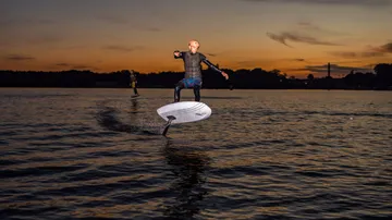 Person, die während des Sonnenuntergangs auf dem Wasser e-foilt.