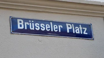 Straßenschild mit der Aufschrift „Brüsseler Platz“ an der Wand.