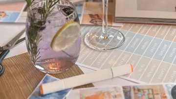 Cocktail with rosemary and lemon on table with magazines.
