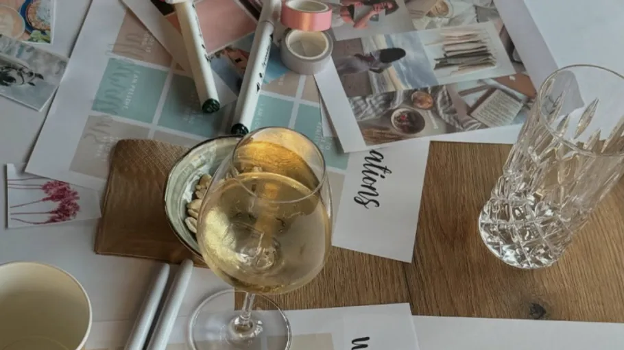 Wine glass on table with photos and pens.