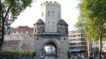 Mittelalterliches Stadttor, umgeben von modernen Gebäuden.