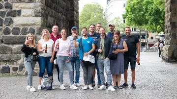Group of people holding drinks under stone archway.