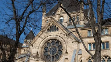 Historisches Gebäude mit großer Rosette, eingerahmt von Bäumen.