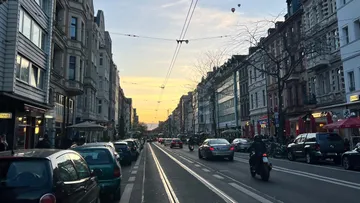 Belebte Straße mit Autos, Gebäuden und Sonnenuntergang.