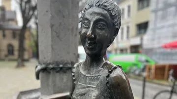 Bronze statue of woman near urban background.