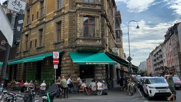 People dining outside a rustic building on a street corner.
