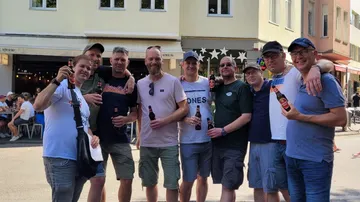 Group of men holding bottles in city street.