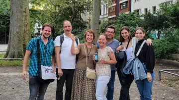 Group of seven people smiling outdoors in park.