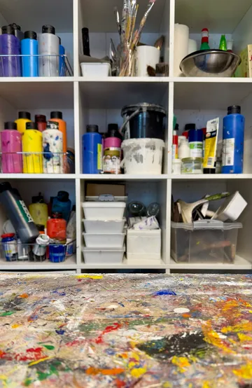 Art supplies on shelves above messy table.