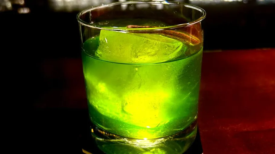 Green cocktail with ice on table.
