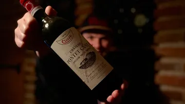 Person holding Château Pontet-Canet wine bottle.