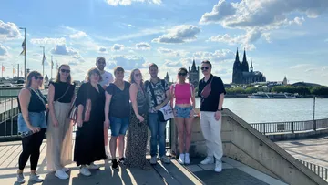 Gruppe posiert in der Nähe eines Flusses, Stadtbild im Hintergrund.