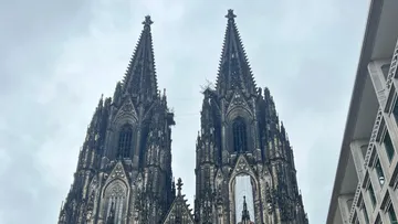 Zwei verzierte gotische Kathedralentürme unter bewölktem Himmel.