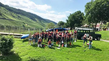 Group of people with paddles by a riverbank.