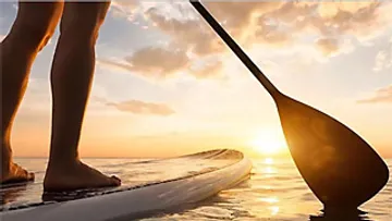 Person paddleboarding at sunset on calm water.