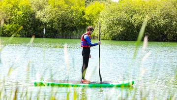 Person beim Paddeln auf einem ruhigen See im Grünen.