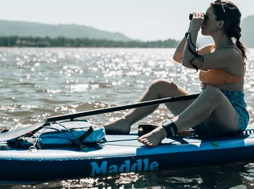 Woman on paddleboard using binoculars on water.