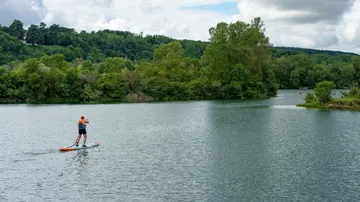 Person paddelt auf einem ruhigen See, umgeben von Bäumen.