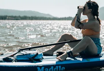 Frau auf dem Paddelbrett mit Fernglas auf dem See.