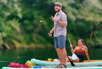 Two people paddleboarding on a calm river.