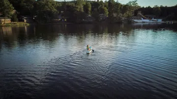 Person paddleboarding on a calm lake with forested shoreline.