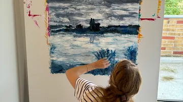 Person painting landscape on large canvas indoors.