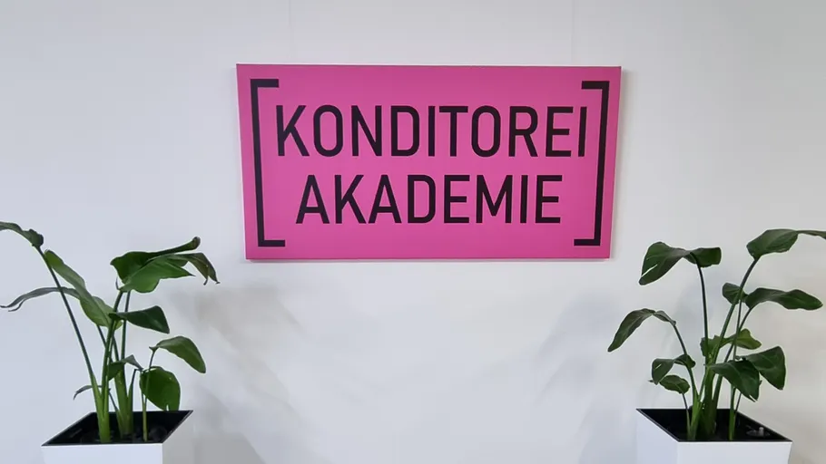 Pink sign reading 'KONDITOREI AKADEMIE' between plants.