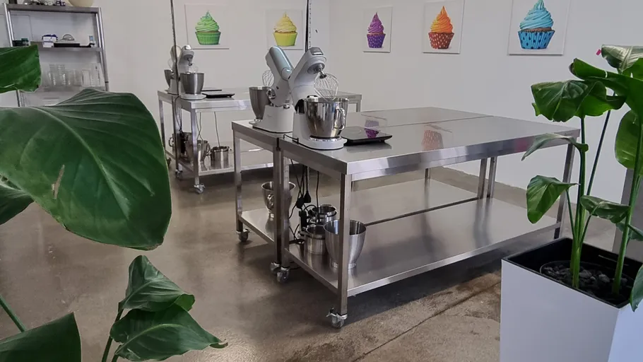Stainless steel kitchen with mixers, plant decor, cupcake art.