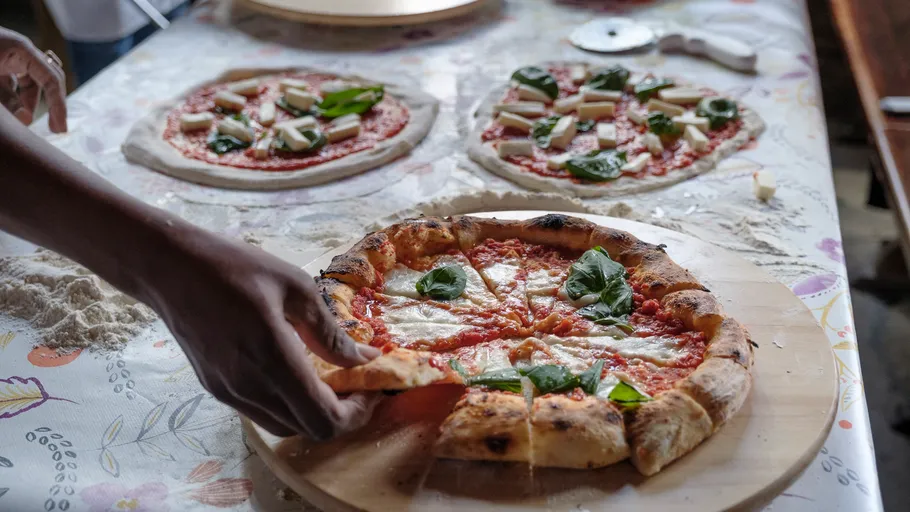 Hand serving freshly baked Margherita pizza indoors.
