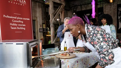 Person, die beim Kochkurs Pizza in den Ofen schiebt.