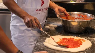 Person spreading sauce on pizza dough.