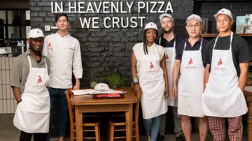 Gruppe von Menschen mit Schürzen in einer Pizzeria.