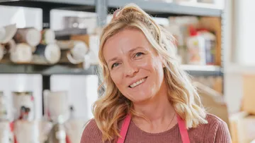 Smiling woman wearing a pink apron, kitchen background.