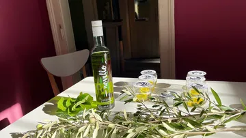 Olive oil bottle and leaves on table.