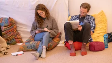Zwei Personen sitzen auf Kissen und schreiben Notizen.