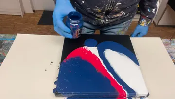 Person, die im Workshop Farbe auf Leinwand gießt.