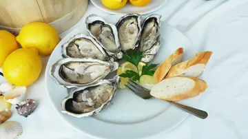 Teller mit Austern, Zitrone, Brot und Petersilie.